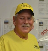 A man in yellow shirt and hat standing next to wall.